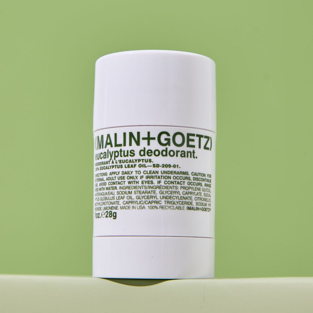 A white cylindrical bottle of Malin+Goetz Eucalyptus Deodorant standing upright against a light green background.